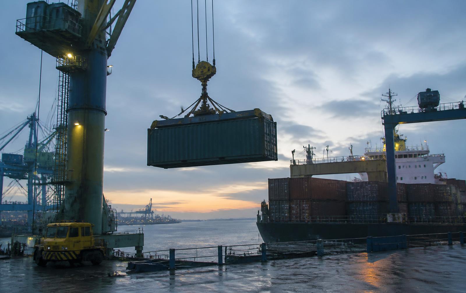 Shipping container being lifted onto a vessel at a port at dawn